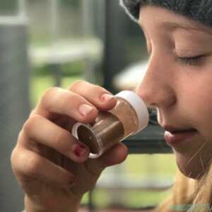 Young person with eyes closed smelling from a small bottle held close to her nose, demonstrating a structured scent-training exercise used to build navigation skills for people with vision impairment.